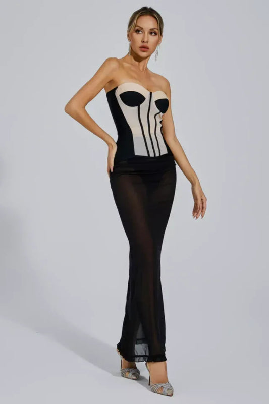 Woman wearing a black and beige strapless corset dress with a sheer black maxi skirt, posing with hands on hips.