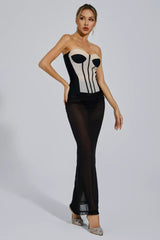 Woman wearing a black and beige strapless corset dress with a sheer black maxi skirt, posing with hands on hips.