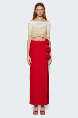 model wearing a red floor-length skirt with a high slit and rose embellishments on the side, paired with a striped crop top