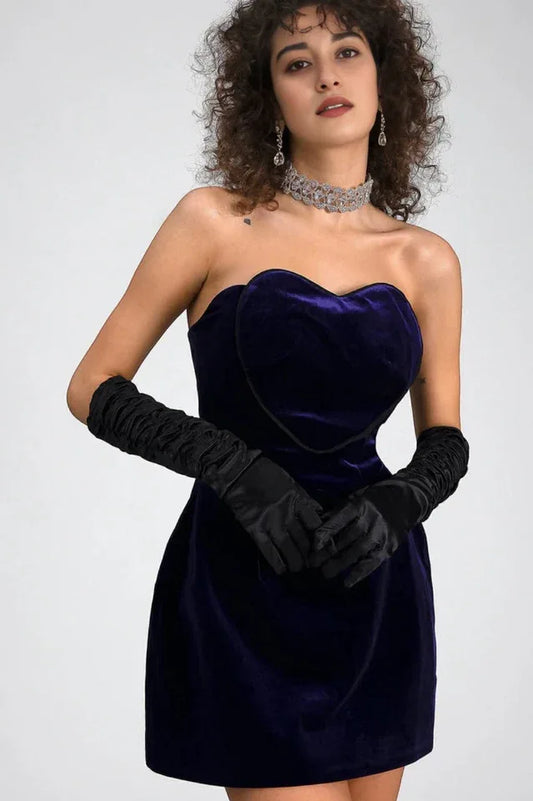 Model wearing a strapless purple velvet mini dress with long black gloves, a jeweled choker, and dangling earrings.