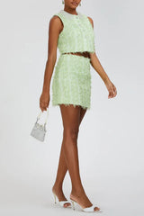 Model walking with a silver mini handbag in a lime green textured tweed crop top and mini skirt set with embellished collar and white heels.