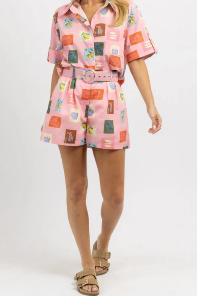 Full body shot of a woman in a pink printed linen blend matching set with short sleeves and high-waisted shorts, accessorized with tan sandals.