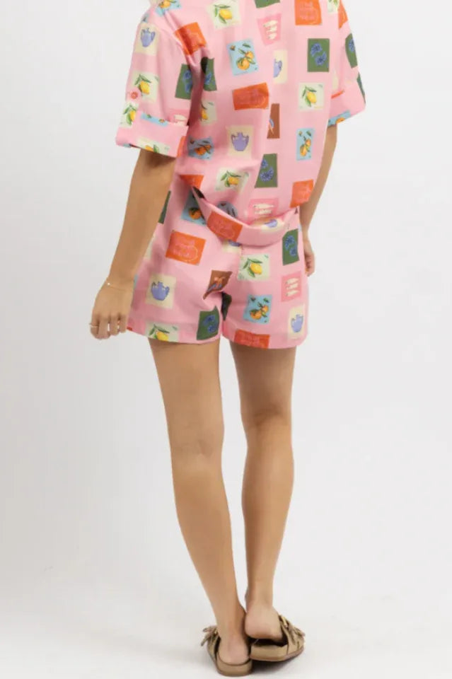 Back view of a woman wearing a pink printed linen blend matching set, showing the short-sleeved shirt and pleated shorts.