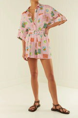 Front view of a woman wearing a pink printed linen blend matching set with a belt, showcasing the button-up shirt and pleated shorts.