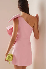 Back view of a pink one-shoulder mini dress with bow embellishments, held by a person with a lime green clutch bag.
