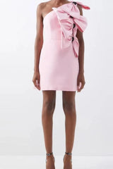 Front view of a pink one-shoulder mini dress with large bow embellishments, held by a person wearing black heels.