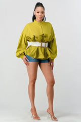 Full-body shot of a woman wearing a lime green peplum top with ruffled detailing, balloon sleeves, and a white belt, paired with denim shorts.