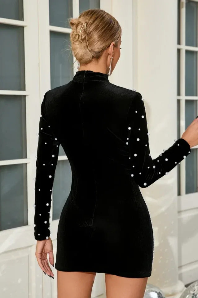 Back view of a black velvet mini dress with a fitted silhouette and pearl embellishments on the sleeves.