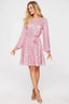 Woman wearing a pink sequined A-line dress with long sleeves and a round neckline, cinched at the waist with a matching belt, paired with silver strappy heels.