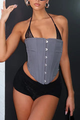 Full body shot of a woman wearing a grey halter corset top with black shorts and black boots.