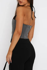 Back view of a woman wearing a grey halter corset top with black pants.
