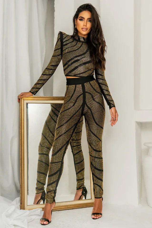 Woman wearing a black and gold rhinestone embellished long-sleeve cropped top and matching high-waisted pants, standing next to a mirror.
