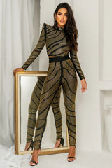 Woman wearing a black and gold rhinestone embellished long-sleeve cropped top and matching high-waisted pants, standing next to a mirror.