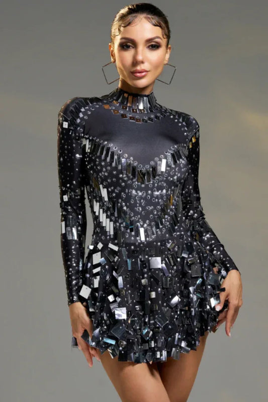 Woman wearing a black long-sleeve mini dress with mirror-like embellishments and a high neckline.