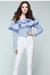 Full-body shot of a woman in a blue and white striped off-the-shoulder ruffled blouse and white pants.