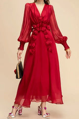 Woman holding a black clutch and wearing a red chiffon dress with floral appliqués and bishop sleeves