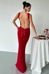 Woman wearing a long red velvet dress with a low back and a large bow detail.
