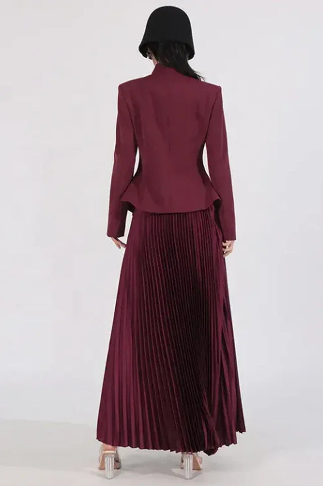 Back view of a woman wearing a burgundy jacket and pleated skirt, with a black hat obscuring her face.