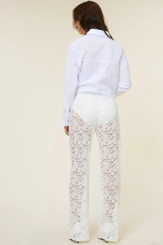 Back view of a woman wearing a white oversized button-down shirt and white lace wide-leg pants.