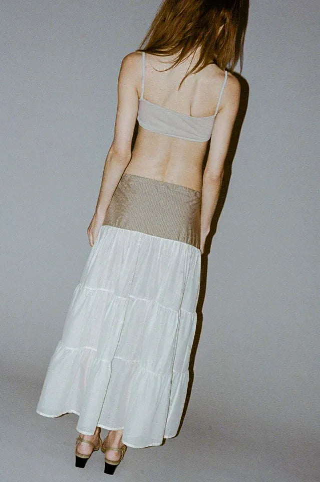 Rear view of a model wearing a light gray crop top and a tiered maxi skirt with a brown pinstripe waistband.