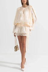 Front view of a woman in a cream mini dress with a draped bodice and ruffled hem.