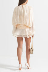 Back view of a woman wearing a cream mini dress with a draped bodice and cinched waist.