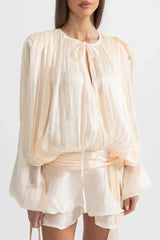 Close-up of the draped bodice and tie neckline of a cream mini dress.