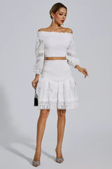 A woman poses in a white smocked crop top and tiered lace skirt, holding a black clutch