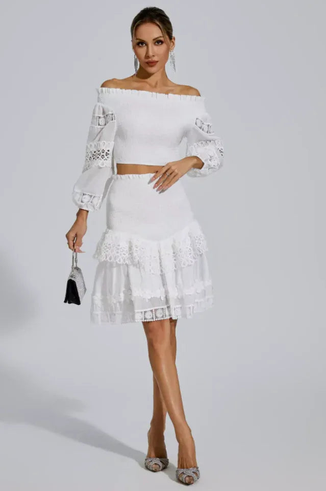 Woman holding a small black purse and wearing a white off-the-shoulder smocked crop top and tiered lace skirt