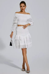 Woman holding a small black purse and wearing a white off-the-shoulder smocked crop top and tiered lace skirt