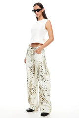 Model wearing a white sleeveless top and wide-leg printed pants, side view with hand in pocket.
