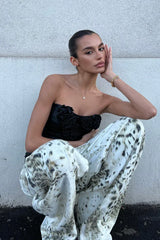 Model wearing a black strapless top and wide-leg printed pants, crouching.