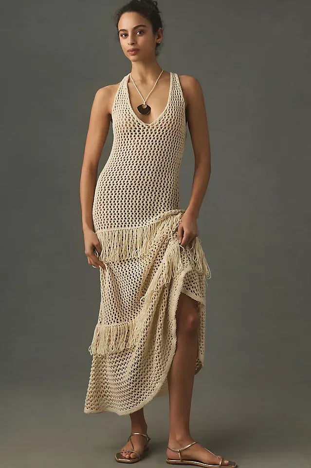 Woman wearing a cream crochet knit maxi dress with fringe details, standing against a grey background.