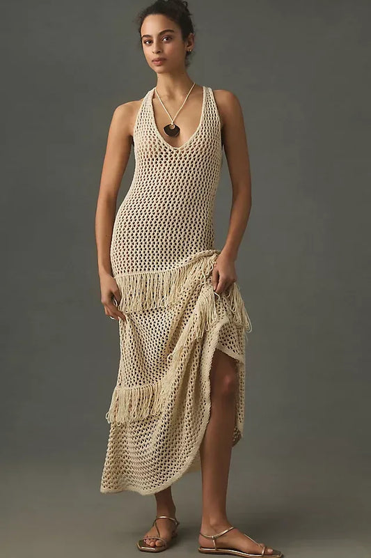 Woman wearing a cream crochet knit maxi dress with fringe details, standing against a grey background.