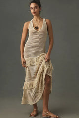 Woman wearing a cream crochet knit maxi dress with fringe details, standing against a grey background.