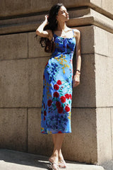 Woman wearing a blue floral print midi slip dress with spaghetti straps, leaning against a stone wall.