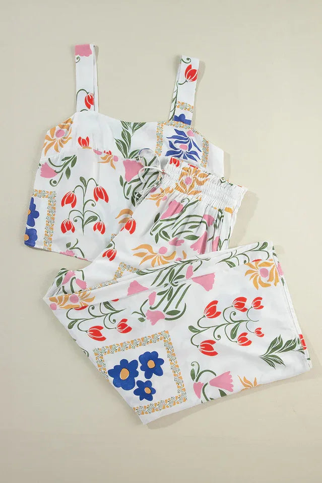 A woman models a white floral print two-piece set, consisting of a square-neck cropped tank top and high-waisted wide-leg pants.