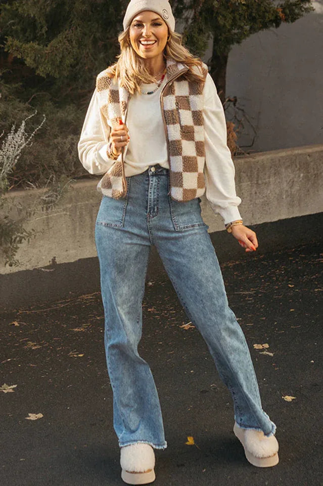 Woman wearing a brown and white checkerboard fleece vest over a white sweatshirt, blue jeans, and fluffy slippers.