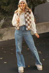 Woman wearing a brown and white checkerboard fleece vest over a white sweatshirt, blue jeans, and fluffy slippers.