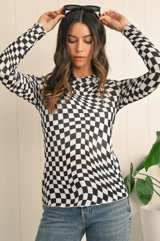 Woman wearing a black and white checkerboard long-sleeved mesh top and blue jeans, holding black sunglasses on her head.