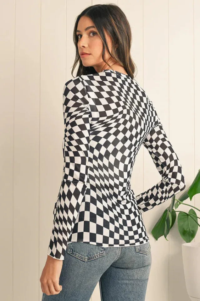 Back view of a woman wearing a black and white checkerboard long-sleeved mesh top and blue jeans.