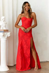 Woman wearing a long red strapless dress with a high leg slit and textured fabric.
