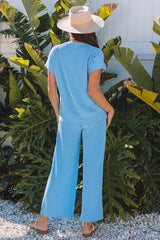 Back view of a woman wearing a blue ribbed short-sleeve top and wide-leg pants with a straw hat and sandals.