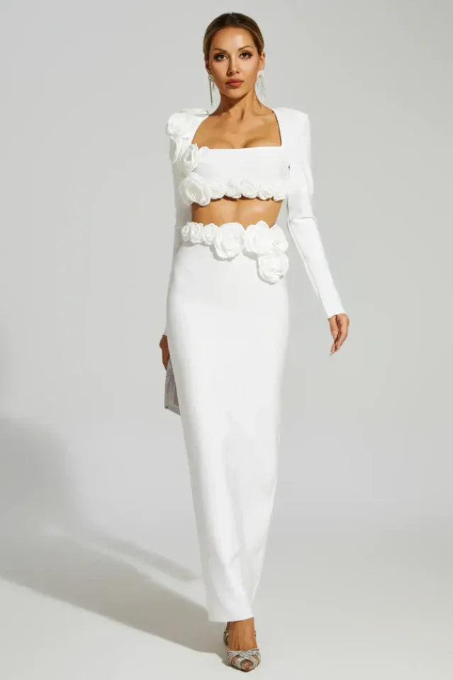 Woman wearing a white two-piece set with long sleeves and a square neckline, adorned with floral embellishments at the shoulders, bust, and waist, paired with a floor-length mermaid skirt.