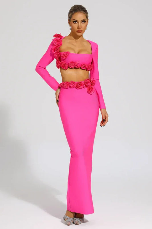 Woman wearing a bright pink two-piece set with long sleeves and a square neckline, adorned with rose embellishments at the shoulders, bust, and waist, paired with a floor-length mermaid skirt with a high slit.