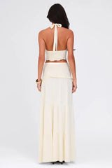 Model wearing a cream-colored two-piece set with a halter neck crop top and a tiered maxi skirt, back view