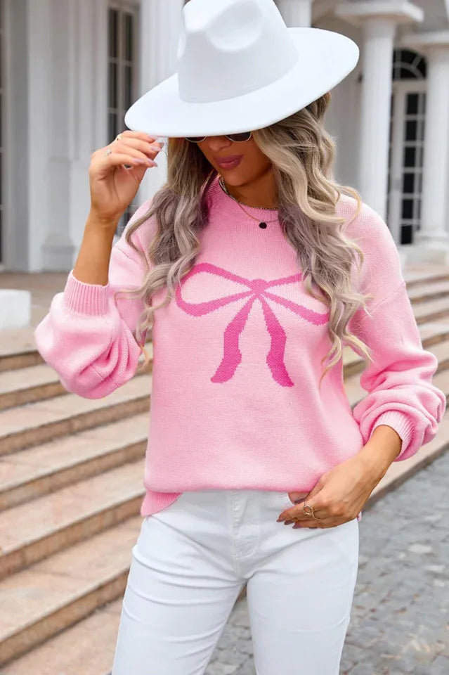 Woman in a pink knit sweater with a bow print, adjusting her sweater.