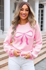 Woman wearing a pink knit sweater with a large pink bow graphic print on the front.