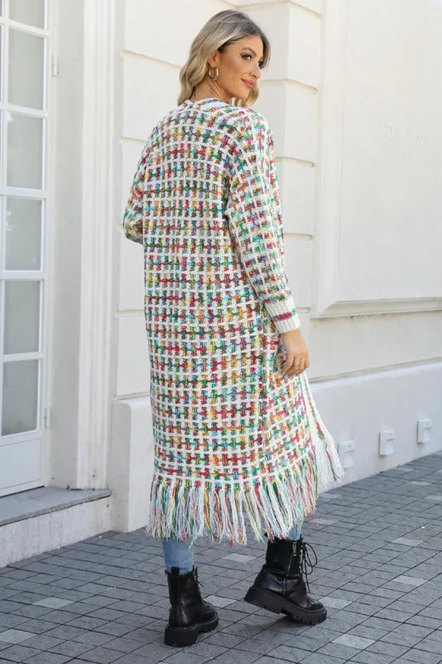 Rear view of a woman wearing a long, multi-colored tweed-inspired knit cardigan with fringe detail, blue jeans, and black boots.