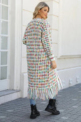 Rear view of a woman wearing a long, multi-colored tweed-inspired knit cardigan with fringe detail, blue jeans, and black boots.